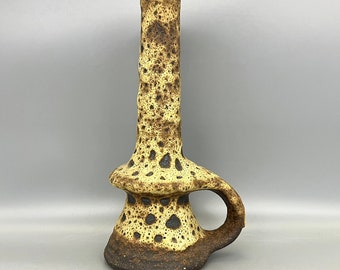 Puede incluir: Un jarrón alto de cerámica con un esmalte moteado marrón y amarillo. El jarrón tiene una forma única, asimétrica, con un asa y una base ancha y acampanada.