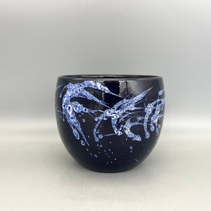 Könnte beinhalten: Ein schwarzer Keramiktopf mit einem weißen und blauen Spritzmuster. Der Topf ist rund und hat eine breite Öffnung.