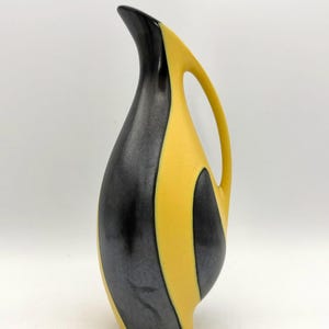 Peut inclure: Une grande carafe en céramique présentant un design bicolore saisissant avec des panneaux verticaux alternés de noir mat et de jaune vif. Le récipient possède un col élancé, une anse incurvée et une forme de corps lisse et arrondie.