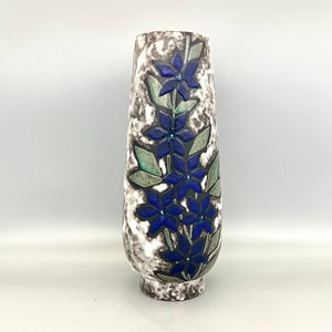 May include: A tall, white ceramic vase with a mottled glaze and a floral design. The vase is decorated with blue and green flowers.