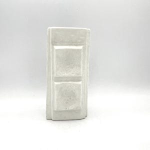 May include: A rectangular, off-white ceramic vase with a textured surface. The vase features a series of recessed panels, creating a geometric design. The neutral color and simple form make it a versatile decorative item.