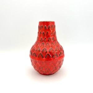Può includere: Un vaso di ceramica rossa con un esterno strutturato a forma di diamante. Il vaso ha un corpo arrotondato e un collo stretto. Il colore è un rosso vibrante con accenti più scuri nelle rientranze a forma di diamante. Il vaso è probabilmente in stile vintage o retrò.