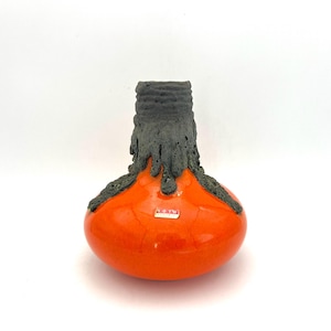 Puede incluir: Un jarrón de cerámica hecho a mano con un cuerpo naranja vibrante y un borde y detalles en gris oscuro texturizado. El jarrón tiene una forma bulbosa y un diseño orgánico único. El jarrón tiene una pequeña etiqueta rectangular.