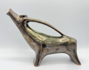 Op de afbeelding: Een keramisch beeld van een antilope met een lange nek en hoorns. Het beeld is geglazuurd in een metallic groene en bruine kleur.