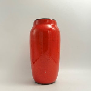 Puede incluir: Un jarrón de cerámica rojo con un borde negro. El jarrón tiene un acabado brillante y una forma ligeramente redondeada.