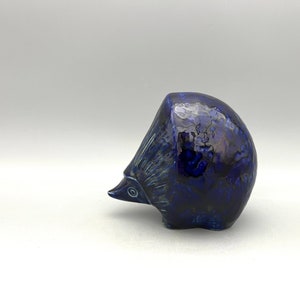 May include: A blue ceramic hedgehog figurine with a textured surface. The figurine is in a curled up position.