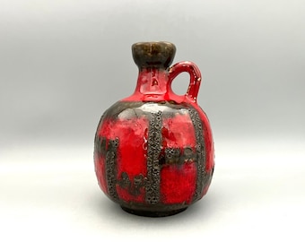 May include: A red and brown ceramic vase with a textured surface and a small handle. The vase has a rounded body and a narrow neck.