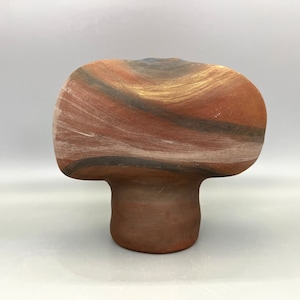 Könnte beinhalten: Eine Keramikvase mit einer einzigartigen, abstrakten Form. Die Vase ist braun mit schwarzen und weißen Streifen, was ihr ein natürliches, erdiges Aussehen verleiht.