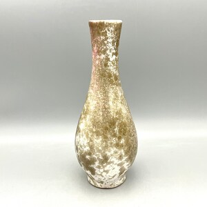 May include: A ceramic vase with a speckled brown and white glaze. The vase has a narrow neck and a rounded body.