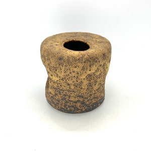 K&ouml;nnte beinhalten: Eine kleine, braune Keramikvase mit einer rauen, strukturierten Oberfl&auml;che. Die Vase hat eine breite &Ouml;ffnung oben und einen etwas schmaleren Boden.