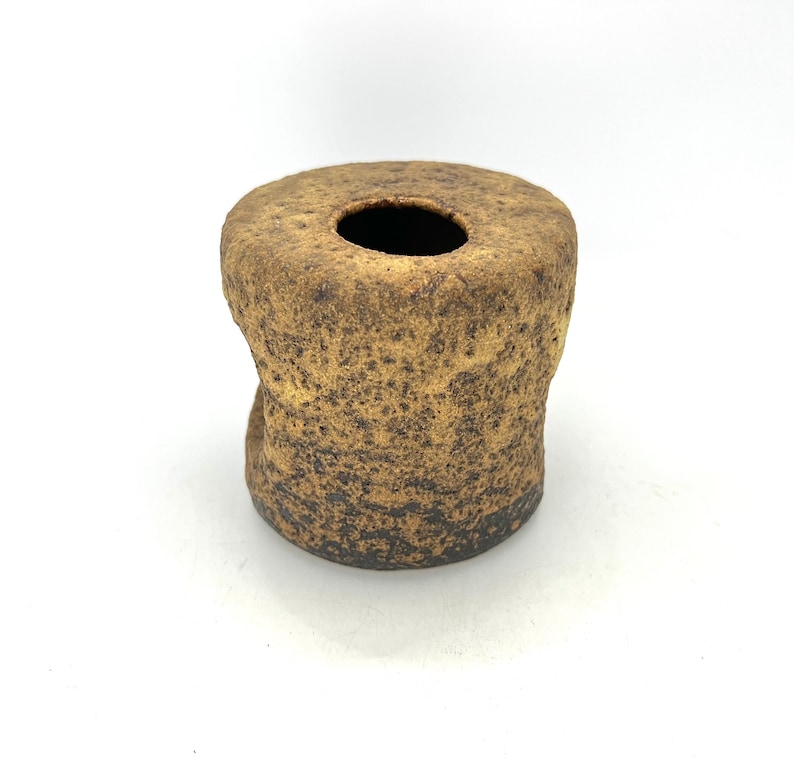 K&ouml;nnte beinhalten: Eine kleine, braune Keramikvase mit einer rauen, strukturierten Oberfl&auml;che. Die Vase hat eine breite &Ouml;ffnung oben und einen etwas schmaleren Boden.
