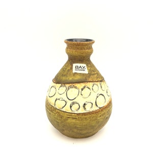 May include: A brown and yellow ceramic vase with a white and black circle pattern. The vase has a label that reads "BAY Keramik".