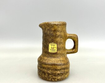 Puede incluir: Una pequeña jarra de cerámica marrón con asa. La jarra tiene una etiqueta que dice "Vest Keramik" con una imagen de un castillo.