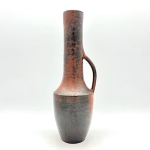 Könnte beinhalten: Eine hohe Keramikvase mit Henkel, die einen Farbverlauf aufweist. Der obere Teil ist rot-orange, der an der Basis in Schwarz übergeht. Die Vase hat einen schlanken Hals und einen gebogenen Henkel, geeignet für Blumengestecke oder dekorative Zwecke.