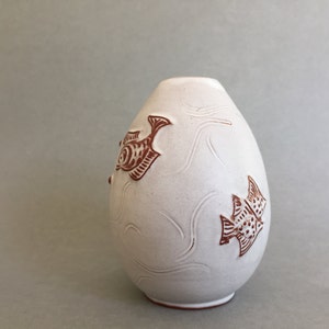 May include: White ceramic vase with a rounded shape and a brown fish design. The vase has a smooth, matte finish.
