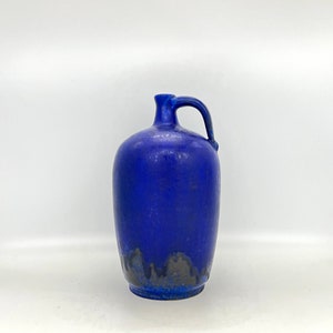 Op de afbeelding: Een blauwe keramische kan met een getextureerd oppervlak en een handvat. De kan heeft een donkerblauwe glazuur met een zilverkleurige glazuur aan de onderkant.