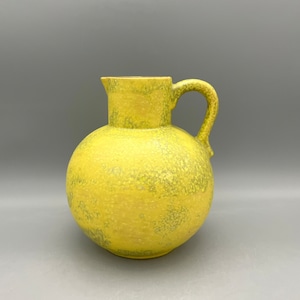 Könnte beinhalten: Eine gelbe Keramikkanne mit einem gesprenkelten Überzug. Die Kanne hat einen runden Körper und einen einzelnen Henkel.