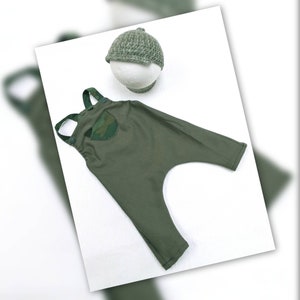 Op de afbeelding: Een groene baby overall met een camouflagezak en een bijpassende groene gebreide muts.