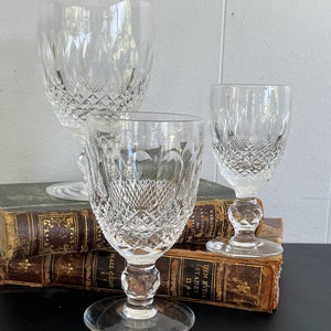 May include: Three clear glass goblets with a diamond pattern on the surface. The goblets are arranged on top of a stack of old books.