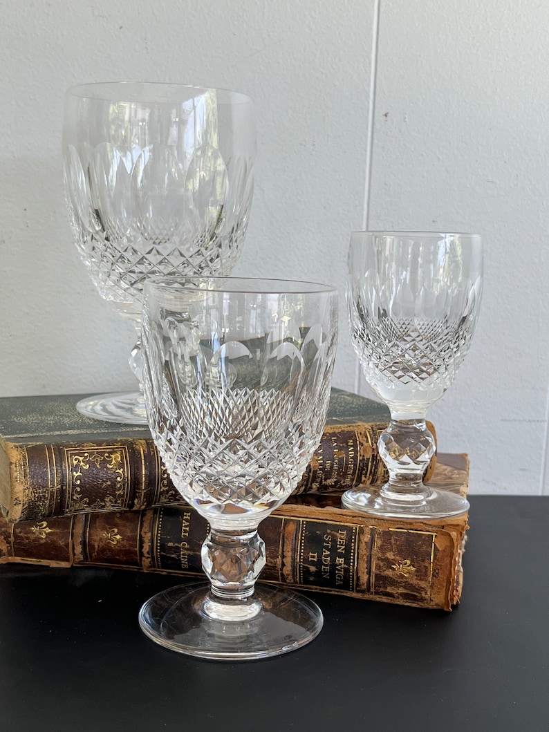 May include: Three clear glass goblets with a diamond pattern on the surface. The goblets are arranged on top of a stack of old books.