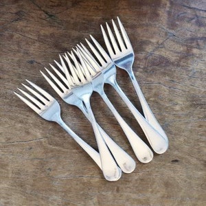May include: A set of six silver forks, arranged in a fan shape, with the tines pointing upwards. The forks are shiny and reflect the light.