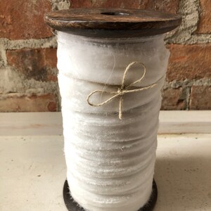 May include: A spool of white velvet ribbon wound around a wooden spool. The ribbon is tied with a natural twine bow.