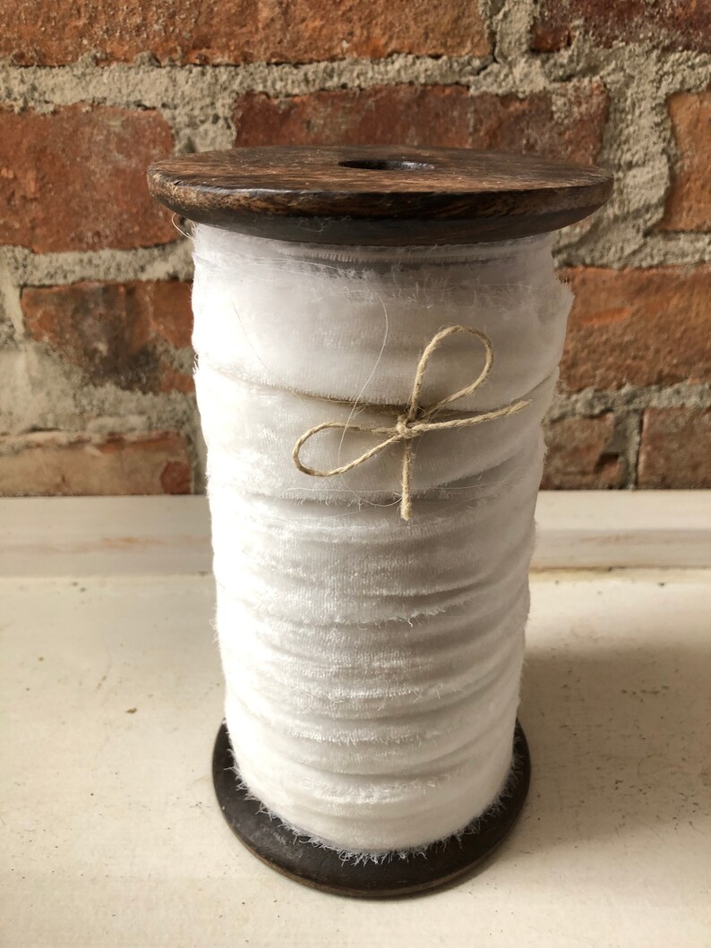 May include: A spool of white velvet ribbon wound around a wooden spool. The ribbon is tied with a natural twine bow.
