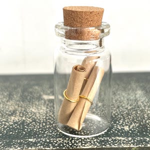 May include: A small glass bottle with a cork stopper, containing a rolled up piece of paper tied with a gold wire.