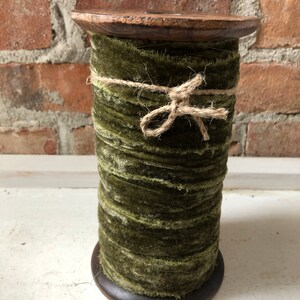 May include: A spool of green velvet ribbon wrapped with twine and tied with a bow. The ribbon is on a wooden spool.