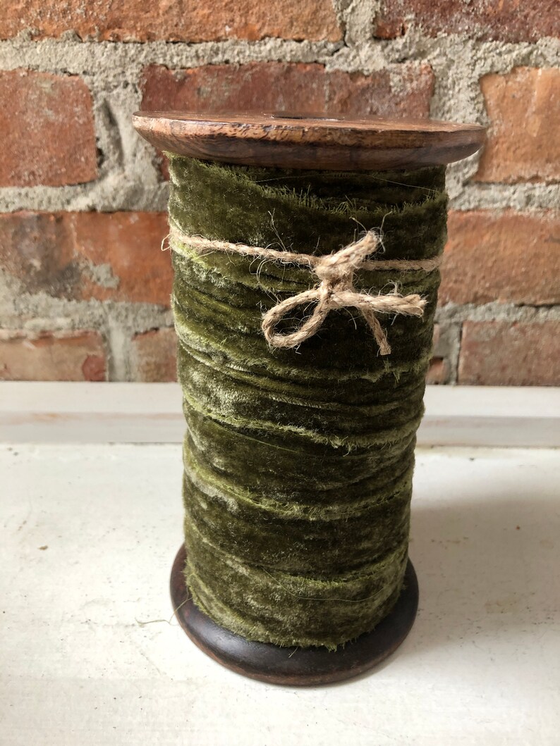 May include: A spool of green velvet ribbon wrapped with twine and tied with a bow. The ribbon is on a wooden spool.