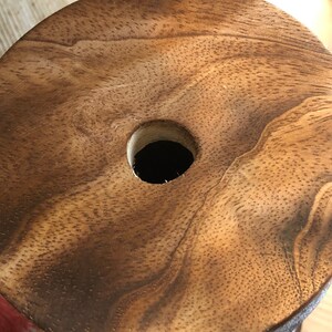 May include: A wooden spool with a hole in the centre. The wood has a natural brown colour and a grainy texture.