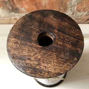 May include: A wooden spool with white string wrapped around it. The spool has a dark brown wood grain and a hole in the centre.