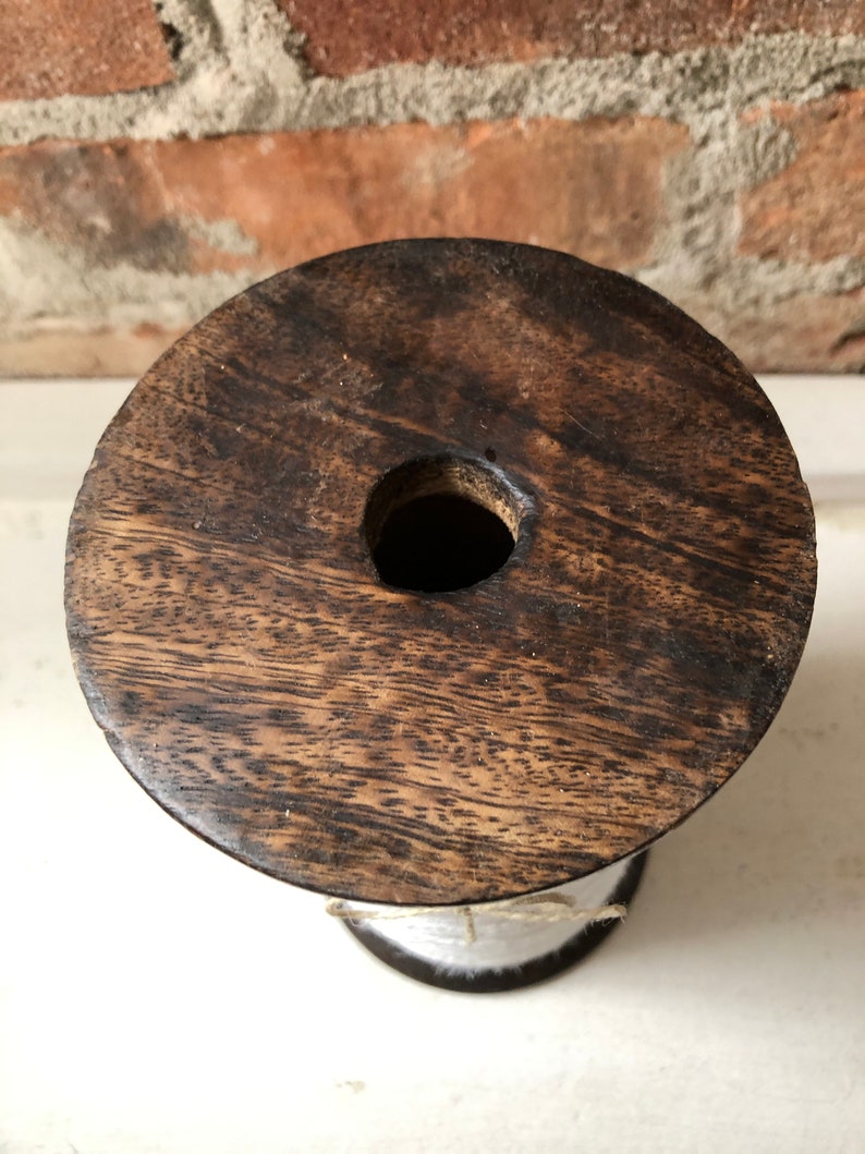 May include: A wooden spool with white string wrapped around it. The spool has a dark brown wood grain and a hole in the centre.