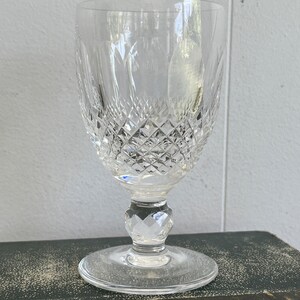 May include: A clear crystal wine glass with a cut diamond pattern. The glass has a tall, slender stem and a wide, round base.