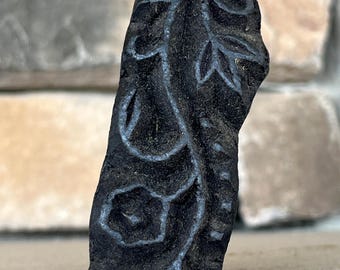 May include: A black carved wooden block with a floral design. The block is used for printing patterns on fabric.