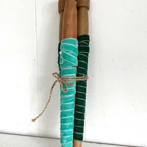 May include: Three wooden dowels wrapped in teal and forest green velvet ribbon. The dowels are tied together with twine.