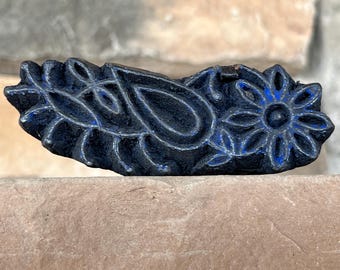 May include: A black wooden block with a carved paisley design and a flower. The block is used for printing patterns on fabric.