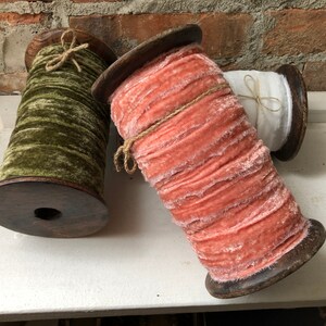 May include: Three spools of fabric ribbon wound on wooden spools. The ribbon is a soft, fuzzy velvet in shades of green, peach, and white.