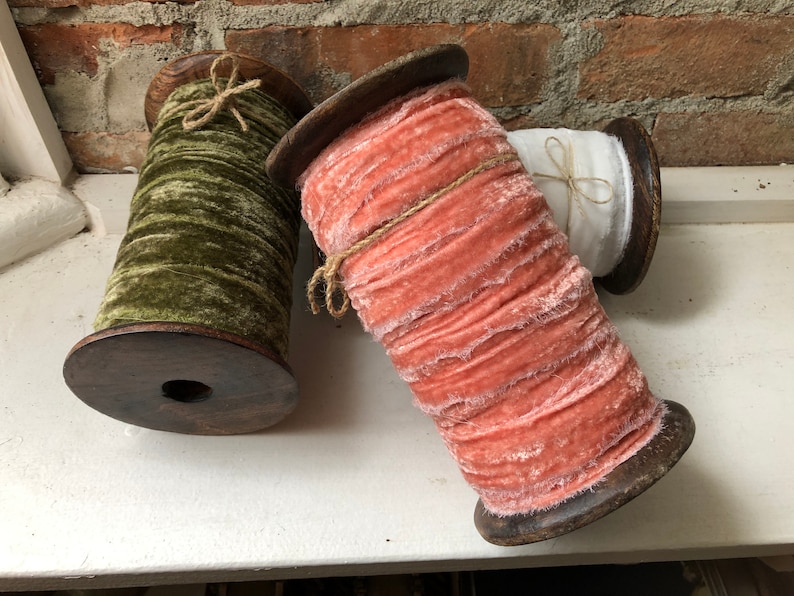 May include: Three spools of fabric ribbon wound on wooden spools. The ribbon is a soft, fuzzy velvet in shades of green, peach, and white.