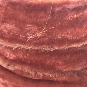 May include: Close-up of a dusty pink velvet fabric with a white thread running through it. The fabric has a soft, plush texture and a subtle sheen.