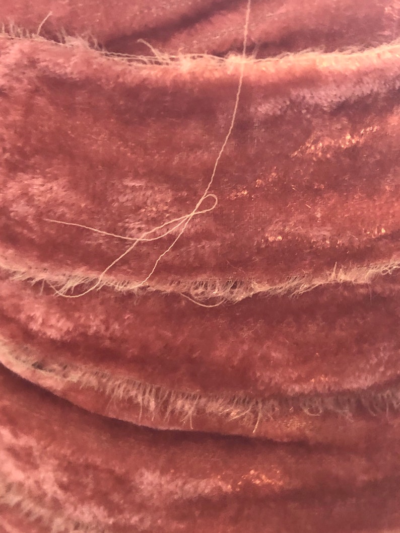 May include: Close-up of a dusty pink velvet fabric with a white thread running through it. The fabric has a soft, plush texture and a subtle sheen.
