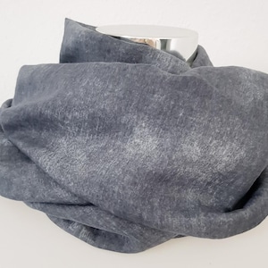 Puede incluir: Una bufanda gris, suave y texturizada hecha de lino. La bufanda está doblada y se muestra en un maniquí.