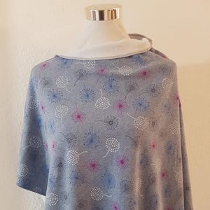 Könnte beinhalten: Ein grauer Poncho mit einem weißen, blauen und pinkfarbenen Löwenzahnmuster.