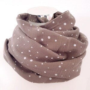 Può includere: Una sciarpa marrone e bianca a pois realizzata in tessuto morbido. La sciarpa è piegata ed esposta su un manichino.