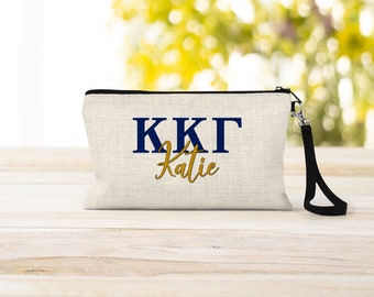 May include: A beige canvas zippered pouch with a black zipper and a black strap. The pouch has the letters "KKG" in navy blue and the name "Katie" in gold lettering.