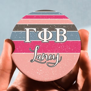 May include: A round coaster with a pink, brown, and blue striped design. The letters "ΓΦΒ" are in white on a pink stripe. The name "Laney" is written in cursive on a pink stripe.