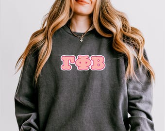 May include: Dark gray sweatshirt with the letters TΦB in pink with a white outline. The sweatshirt is a crew neck style and has a vintage, washed look. The letters are in a bubble font.