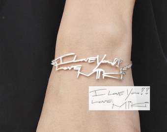 May include: Silver bracelet with a handwritten inscription that reads "I love you so Love, Mik" on a white note.