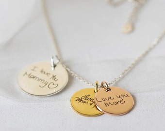 May include: A silver chain necklace with three round pendants. The pendants are silver, gold, and rose gold. Each pendant has handwritten text. The silver pendant says "I love you mommy" with a heart. The gold pendant says "Love Mom" and the rose gold pendant says "Love you more".