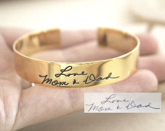 May include: Gold bangle bracelet with the inscription "Love Mom & Dad" in black cursive handwriting.